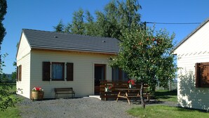 Un petit bâtiment d’un seul étage, doté d’un toit en pente, d’une allée en gravier et d’un banc en bois à l’extérieur.
