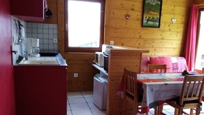Une cuisine compacte équipée d’un évier, d’un four à micro-ondes et d’un petit réfrigérateur. On y trouve également un coin repas avec une table et des chaises, ainsi qu’une fenêtre qui laisse entrer la lumière naturelle.