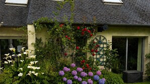 A house with a garden featuring white and purple flowers, a green door, and a window with a green frame. - Peaceful house between sea and forest near Perros-Guirec (Louannec)