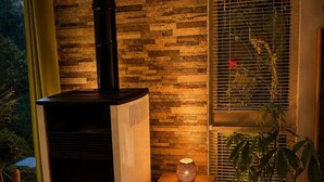 A wood-burning stove with a chimney, a window with blinds, and a potted plant. - Peaceful house between sea and forest near Perros-Guirec (Louannec)