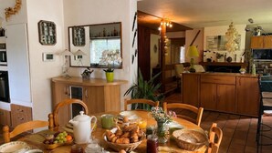 A dining area with a wooden table set for breakfast, a kitchen in the background, and a chandelier. - Peaceful house between sea and forest near Perros-Guirec (Louannec)