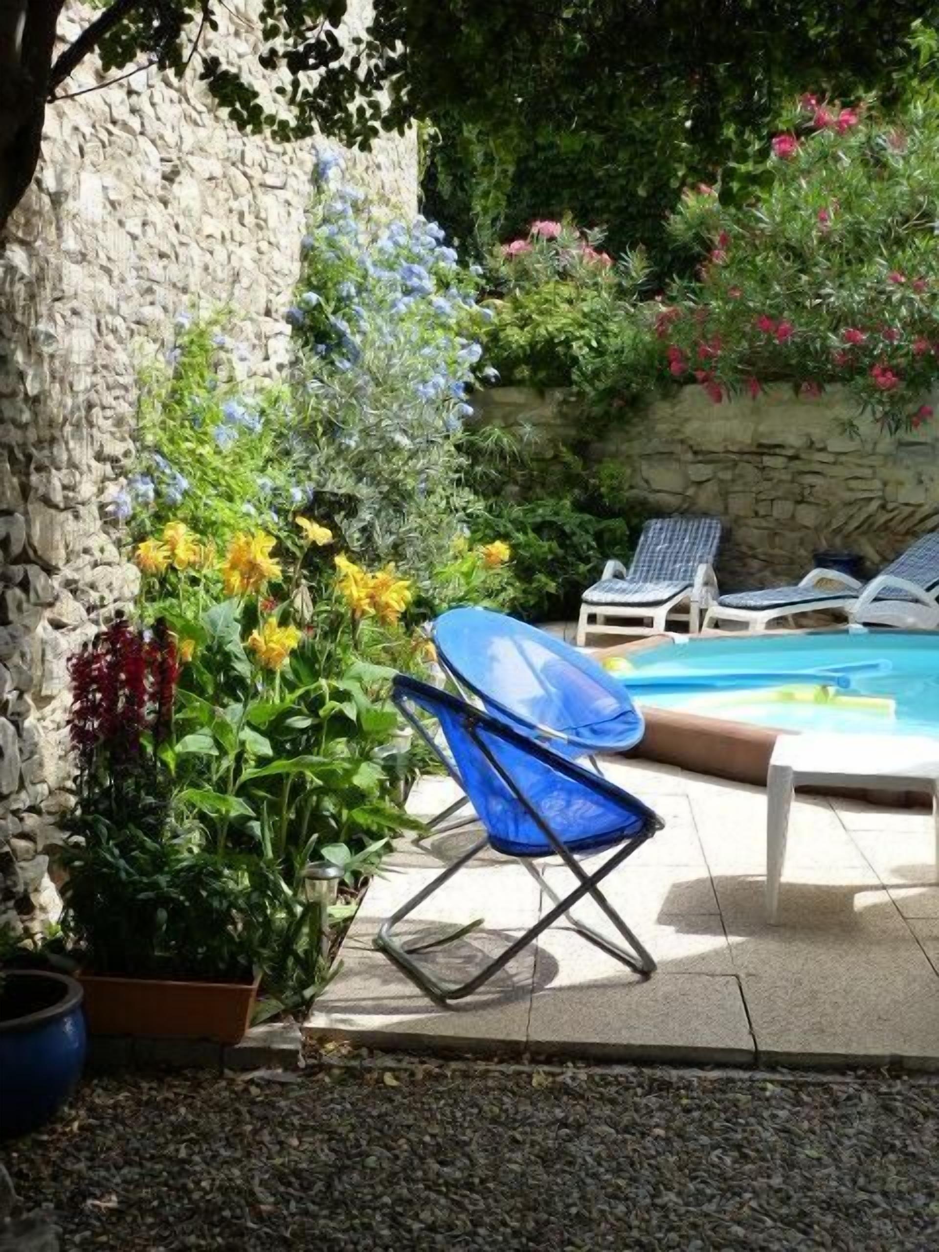 Un espace aménagé au bord de la piscine, avec des chaises longues, une chaise pliante bleue et diverses plantes.