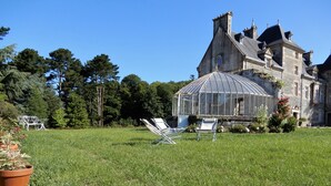 Ein großes Steinhaus mit Wintergarten, umgeben von gepflegtem Rasen und Bäumen.