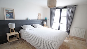 Une chambre à coucher avec un lit, des tables de chevet, une lampe, un tableau et une fenêtre avec des rideaux.