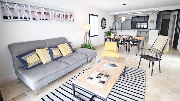 Un salon moderne avec un canapé gris, des coussins jaunes et bleus, un tapis à rayures et une table basse sur laquelle sont posés des magazines.