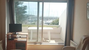 A cozy living room with a wooden ceiling, a sofa, a coffee table, and a TV on a wooden stand. There is a balcony with a view of the city. - Sea view apartment La trinité sur mer (La Trinité-Sur-Mer)