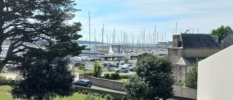 A marina with numerous boats docked, a parking area with cars, and a stone building with a sloped roof.