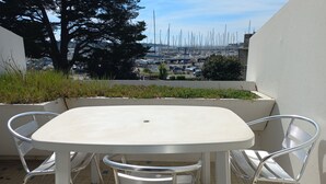 A white table and four metal chairs on a tiled patio with a view of a marina and buildings in the background. - Sea view apartment La trinité sur mer (La Trinité-Sur-Mer)