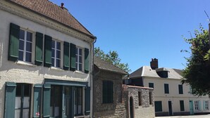 Une rue bordée d’immeubles aux façades en pierre et aux volets verts.