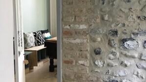 Une pièce avec un mur en pierre, un banc en bois et un lit agrémenté d’oreillers à motifs.