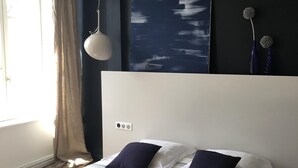 Une chambre à coucher moderne avec un lit, une grande peinture abstraite et un luminaire suspendu.