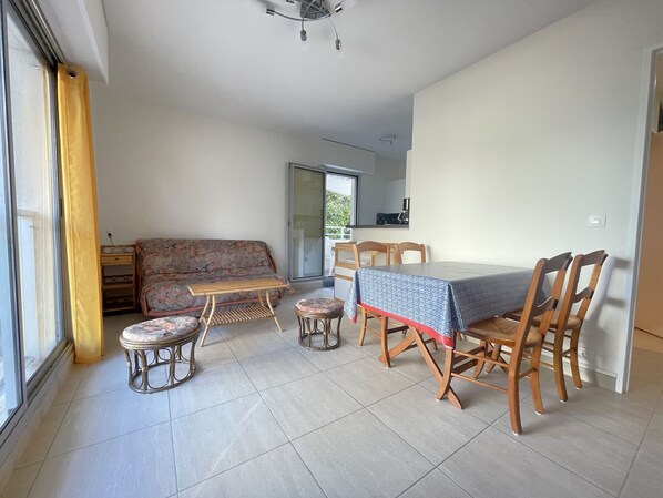 Una sala de estar con sofá, una mesa de centro, una mesa de comedor con sillas y una cocina visible a través de una puerta de vidrio.