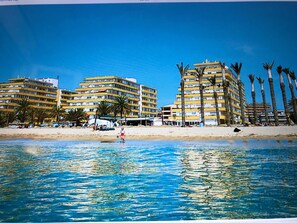 A beachfront hotel with multiple balconies, palm trees, and a sandy beach.
