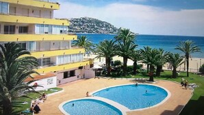 Een hotel met een zwembad, palmbomen en uitzicht op zee.