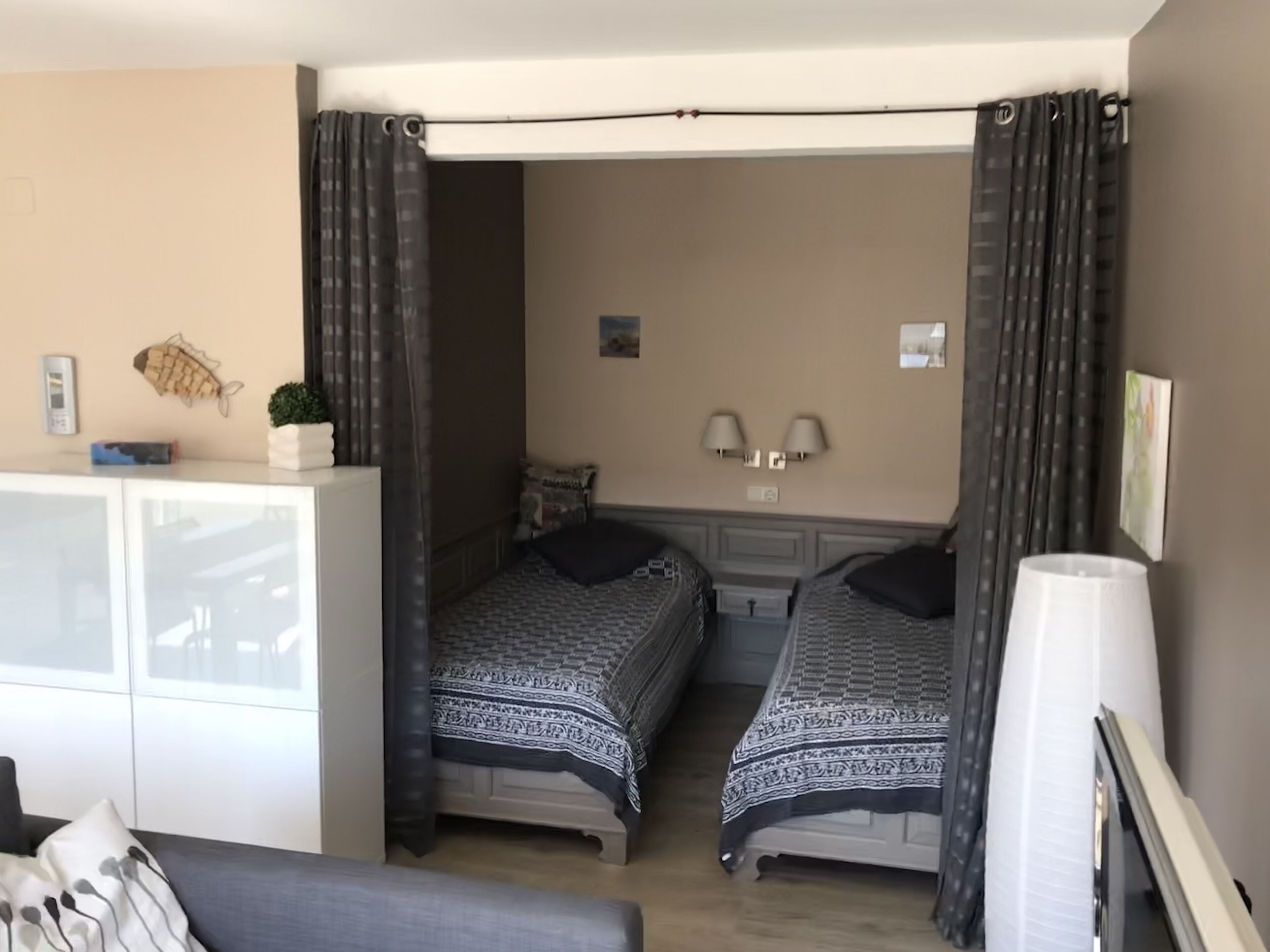 A room with two beds, a desk, a lamp, and a wall-mounted light fixture.