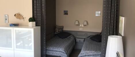 A room with two beds, a desk, a lamp, and a wall-mounted light fixture.