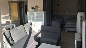 Een moderne hotelkamer met een grijze bank, een wit kastje, een bed met gestreept beddengoed en een televisie.