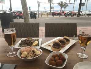 A table with food and drinks, overlooking a street with parked cars and palm trees.