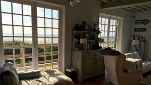 A cozy living room with a large window overlooking a beach, a bookshelf, and a sign indicating directions to the garden and beach. - Typical Norman house on the beach - sea view - big garden - perfect location (Benerville-Sur-Mer)