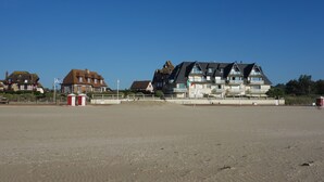 A beachfront property with a large building featuring multiple balconies, a sandy beach in the foreground, and a clear blue sky. - Typical Norman house on the beach - sea view - big garden - perfect location (Benerville-Sur-Mer)