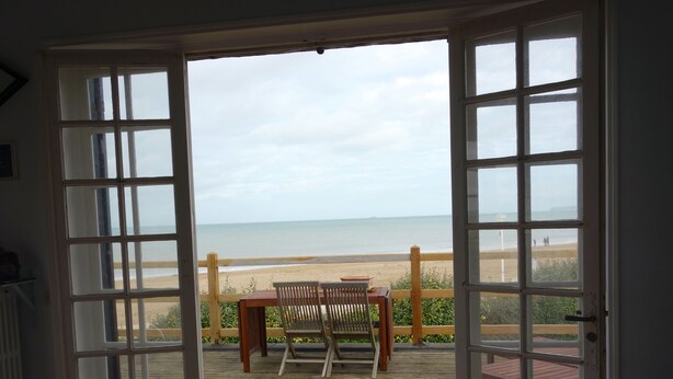 An open door leading to a wooden deck with a table and chairs, overlooking a beach. - Typical Norman house on the beach - sea view - big garden - perfect location (Benerville-Sur-Mer)