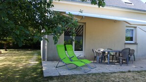 A patio area with a table and chairs, a green lounge chair, and a covered seating area. - House on the heights of Dinard, 900 m from the beach in a quiet subdivision. (Dinard)