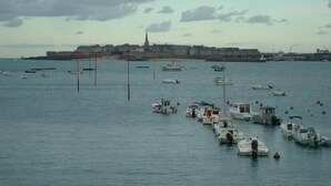 A marina with various boats docked, a distant city skyline, and a cloudy sky. - House on the heights of Dinard, 900 m from the beach in a quiet subdivision. (Dinard)