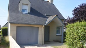 A residential house with a grey garage door, a stone-paved driveway, and a well-maintained lawn. - House on the heights of Dinard, 900 m from the beach in a quiet subdivision. (Dinard)