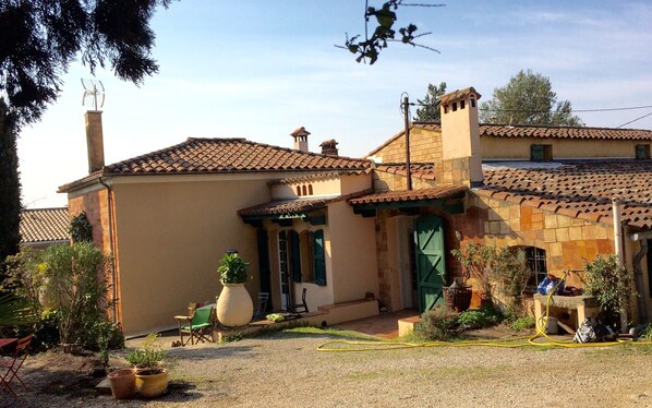 A house with a tiled roof, a chimney, and a garden with potted plants and a hose.