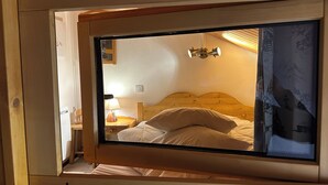 A bedroom with a wooden headboard, a bed with white bedding, a nightstand with a lamp, and a window with a view of a mountain. - Duplex, 2 rooms + Cabin in Tignes, ski-in/ski-out, family area (Tignes)