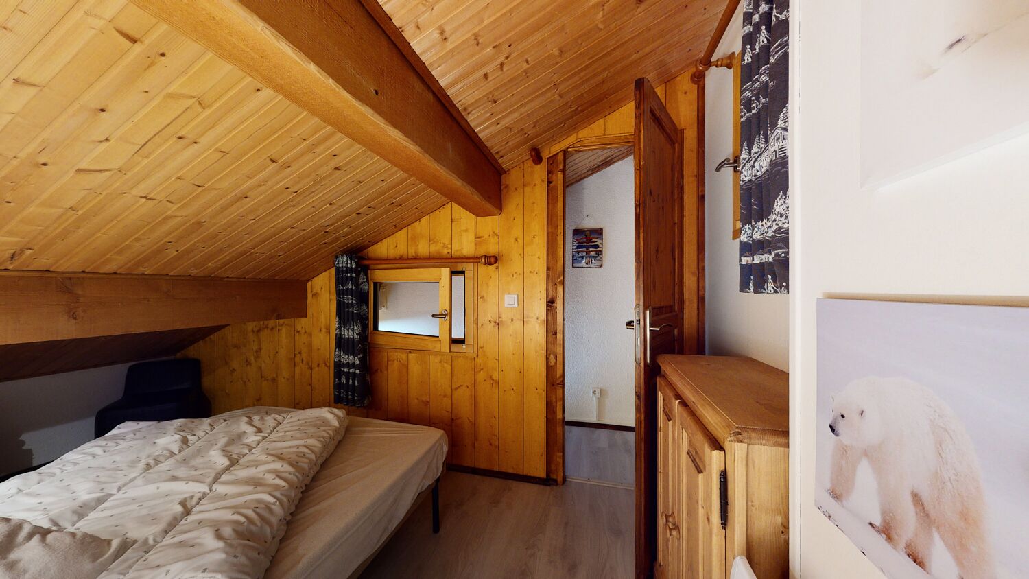 Ein Zimmer in einer Holzhütte mit einem Bett, einem Holzschrank und einer Tür zu einem weiteren Raum.