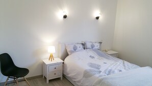 Ett sovrum med en säng, sängbord, en lampa, en stol och väggmonterade lampor.