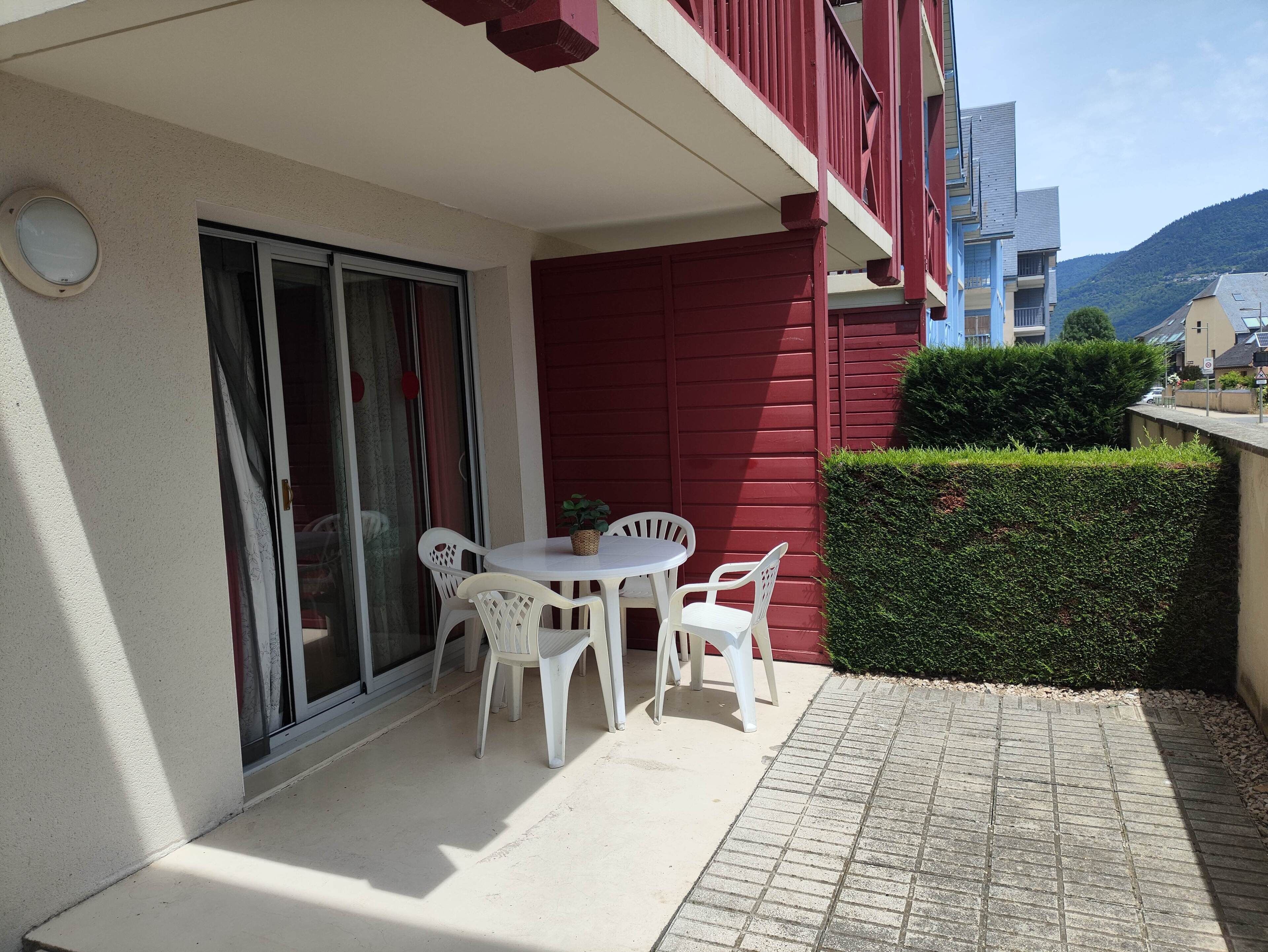 A balcony with a table and chairs, a potted plant, and a red wall.