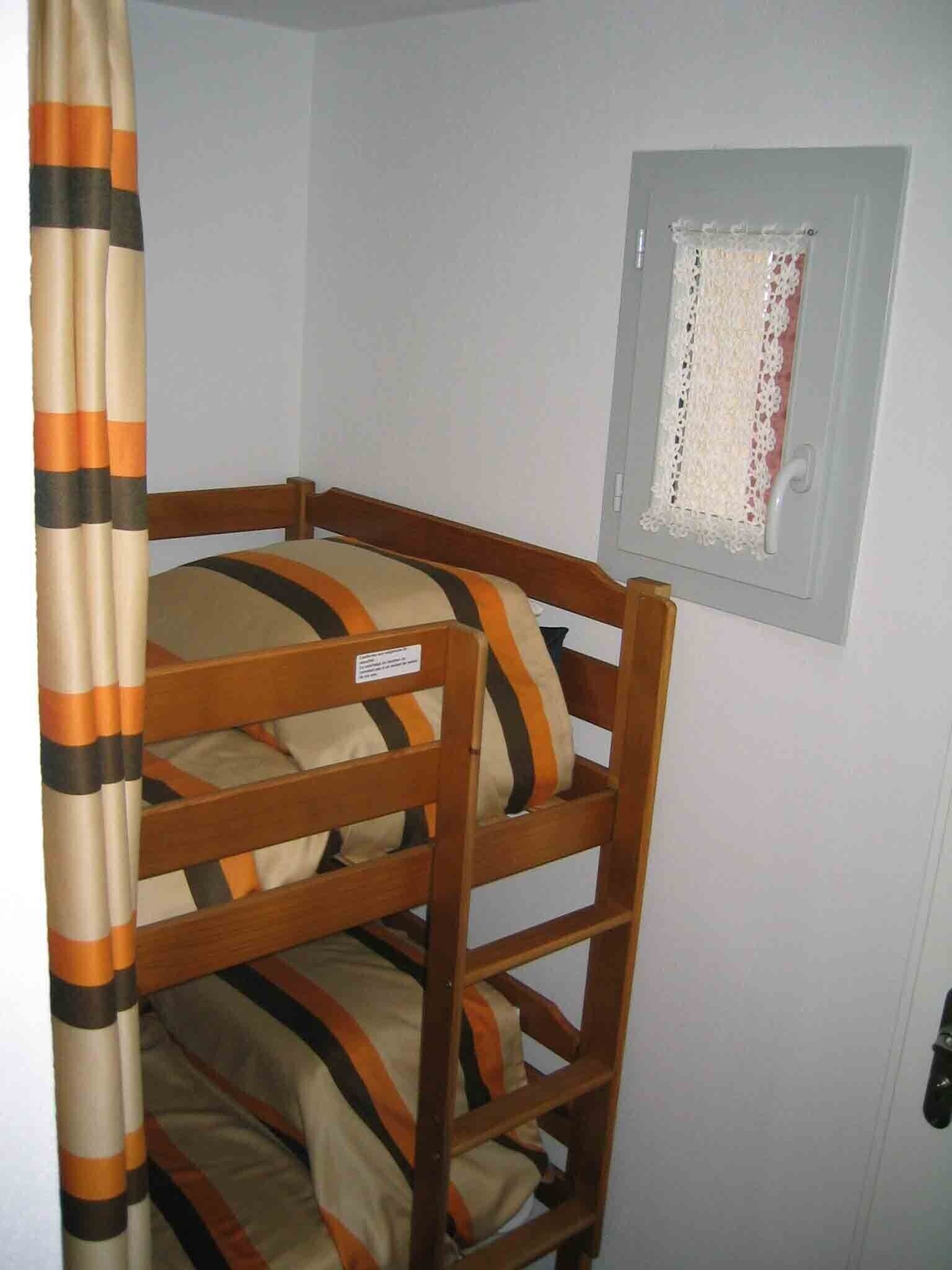 Una cama litera con ropa de cama a rayas, un cabecero de madera y una ventana con cortinas de encaje.