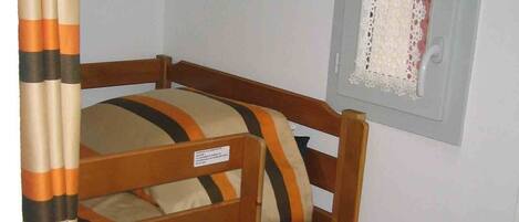 Una cama litera con ropa de cama a rayas, un cabecero de madera y una ventana con cortinas de encaje.