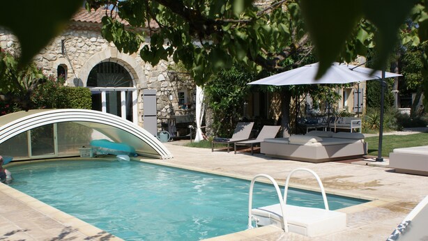 Una piscina con trampolín, sillas de descanso y una zona de estar techada.