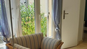 Un sofá de mimbre con cojines a rayas en una habitación con un ventanal corredero que da a un jardín.