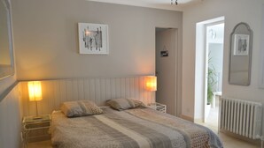 Un dormitorio con cama, lámparas de noche, un radiador y una puerta que da a otra habitación.