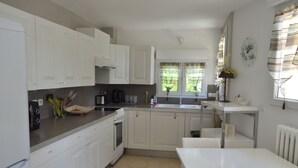Una cocina moderna con armarios blancos, horno empotrado y zona de comedor con una mesa blanca.