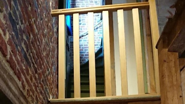 Una escalera de madera con barandilla que conduce a un muro de ladrillo y una ventana con vista a un edificio de ladrillo.