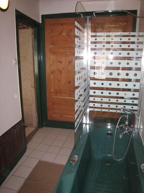 A bathroom with a glass-enclosed bathtub, a wooden door, and a tiled floor.