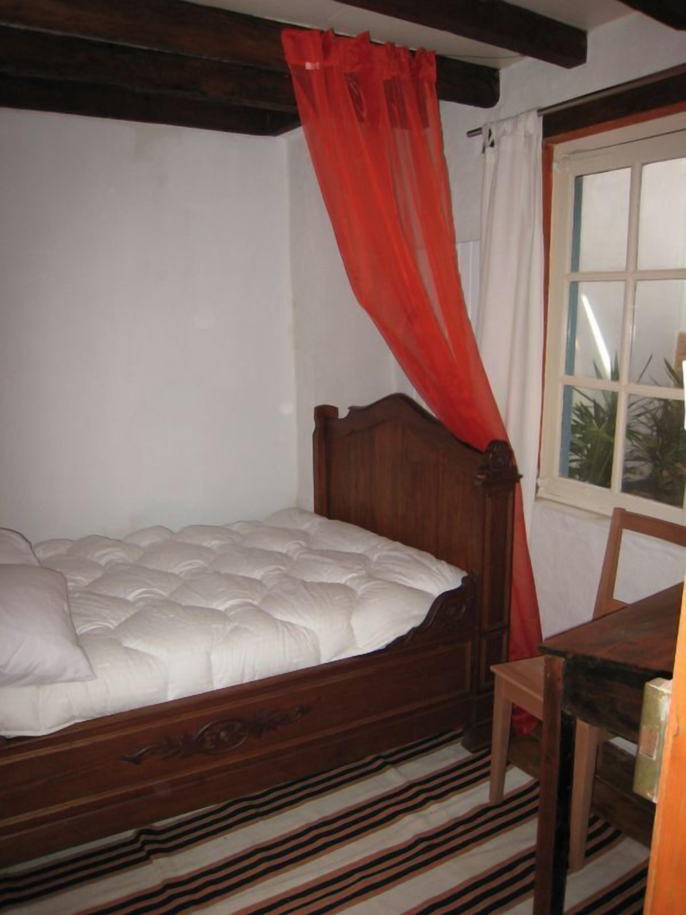 A single bed with a wooden headboard, a red curtain, and a striped rug.