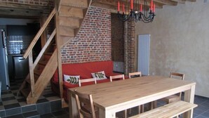 Un comedor con mesa de madera y bancos, pared de ladrillo, escalera y un banco con cojines rojos.