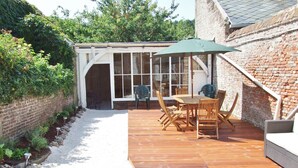 A wooden deck with a table and chairs, a covered patio area, and a brick wall. - From 98€/jour, 5mns walk to fine sand at M Basse, Jard, 7pers+BB, heating included (Veules-Les-Roses)