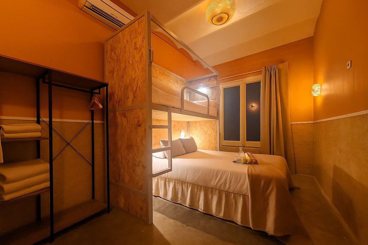 A compact hotel room with a bunk bed, a wardrobe, a bedside table with a lamp, and a window with curtains.