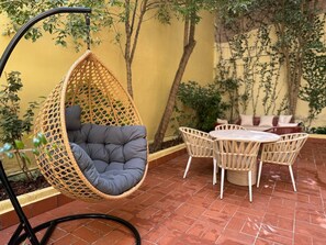 A hanging chair with a cushioned seat and back, a round table with chairs, and a tiled patio area. - The Loft House Barcelona (Barcelona)