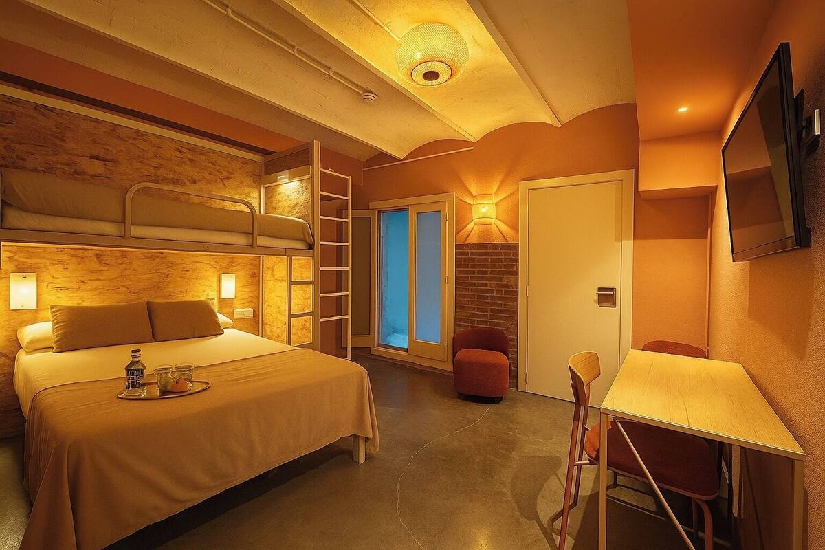 A hotel room with a bunk bed, a desk with a chair, a small table with a lamp, and a sliding door leading to a bathroom.