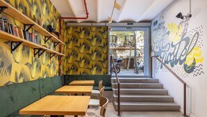 A cafe with wooden tables and green cushioned seating, a staircase leading to an outdoor area, and a mural on the wall. - The Loft House Barcelona (Barcelona)