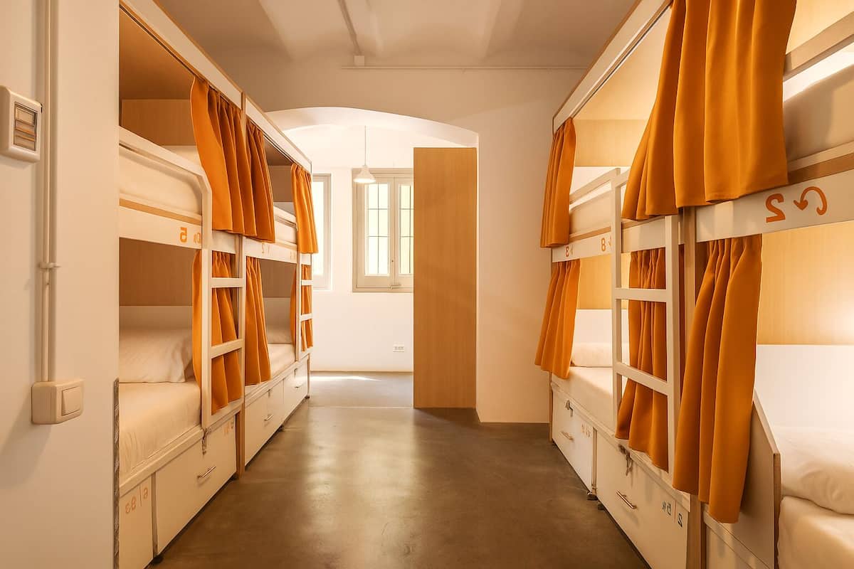 A narrow corridor with bunk beds on both sides, a door at the end, and a window with natural light.