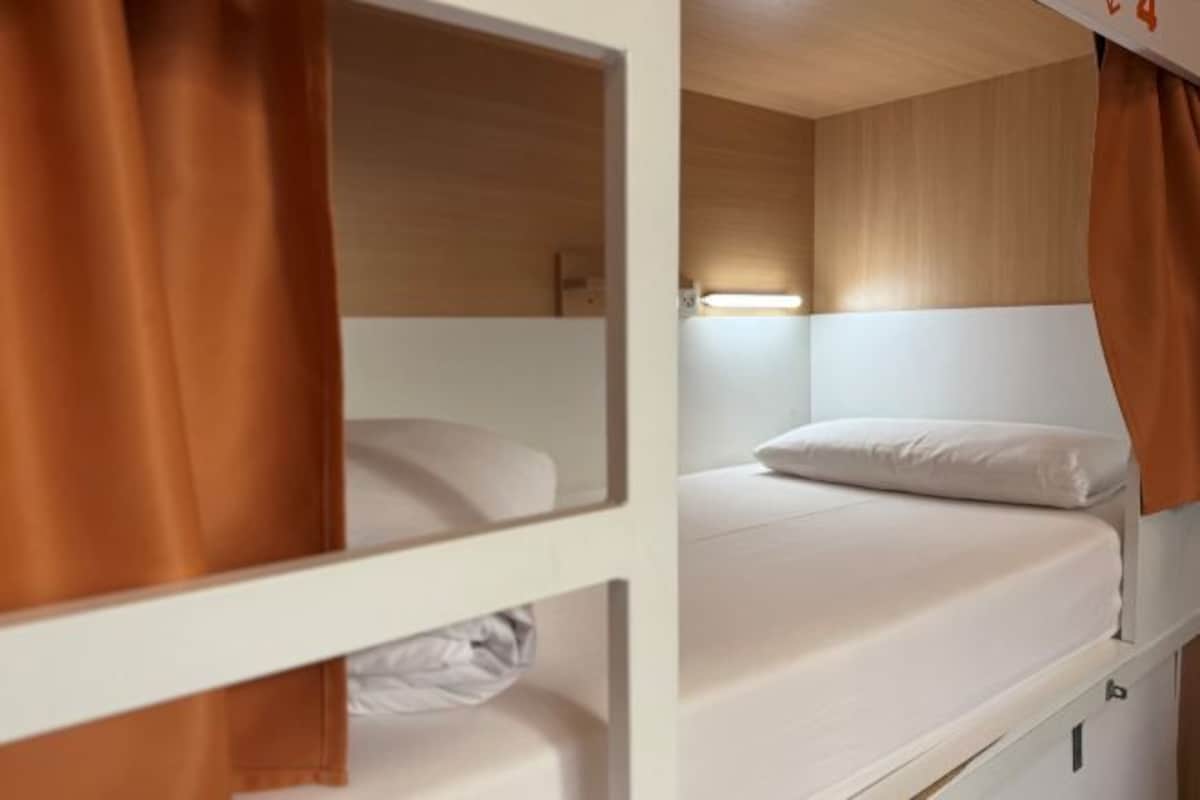 A bunk bed with a white mattress and a single pillow. There is a wooden headboard and a small shelf below the bed.